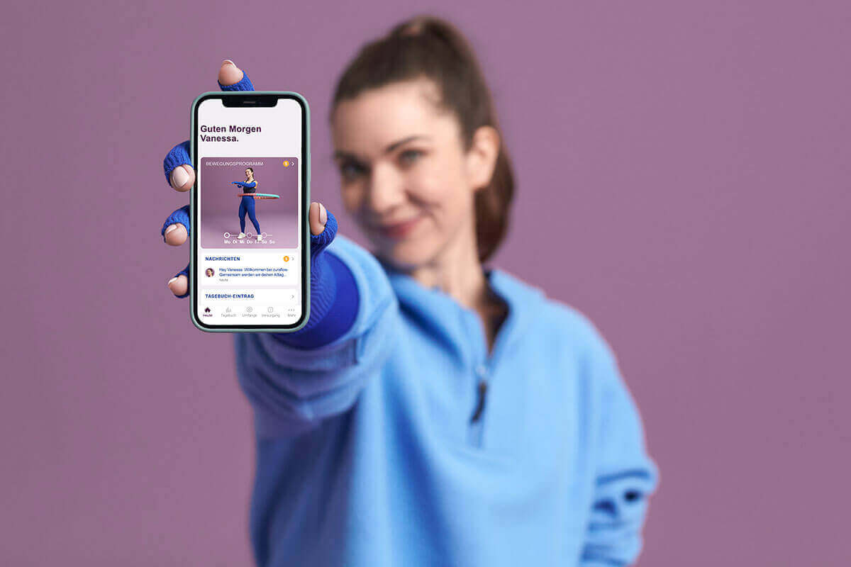 Afgebeeld is een vrouw die haar smartphone met de Bauerfeind curaflow-app toont. De app ondersteunt mensen met lip- en lymfoedeem bij hun behandeling.