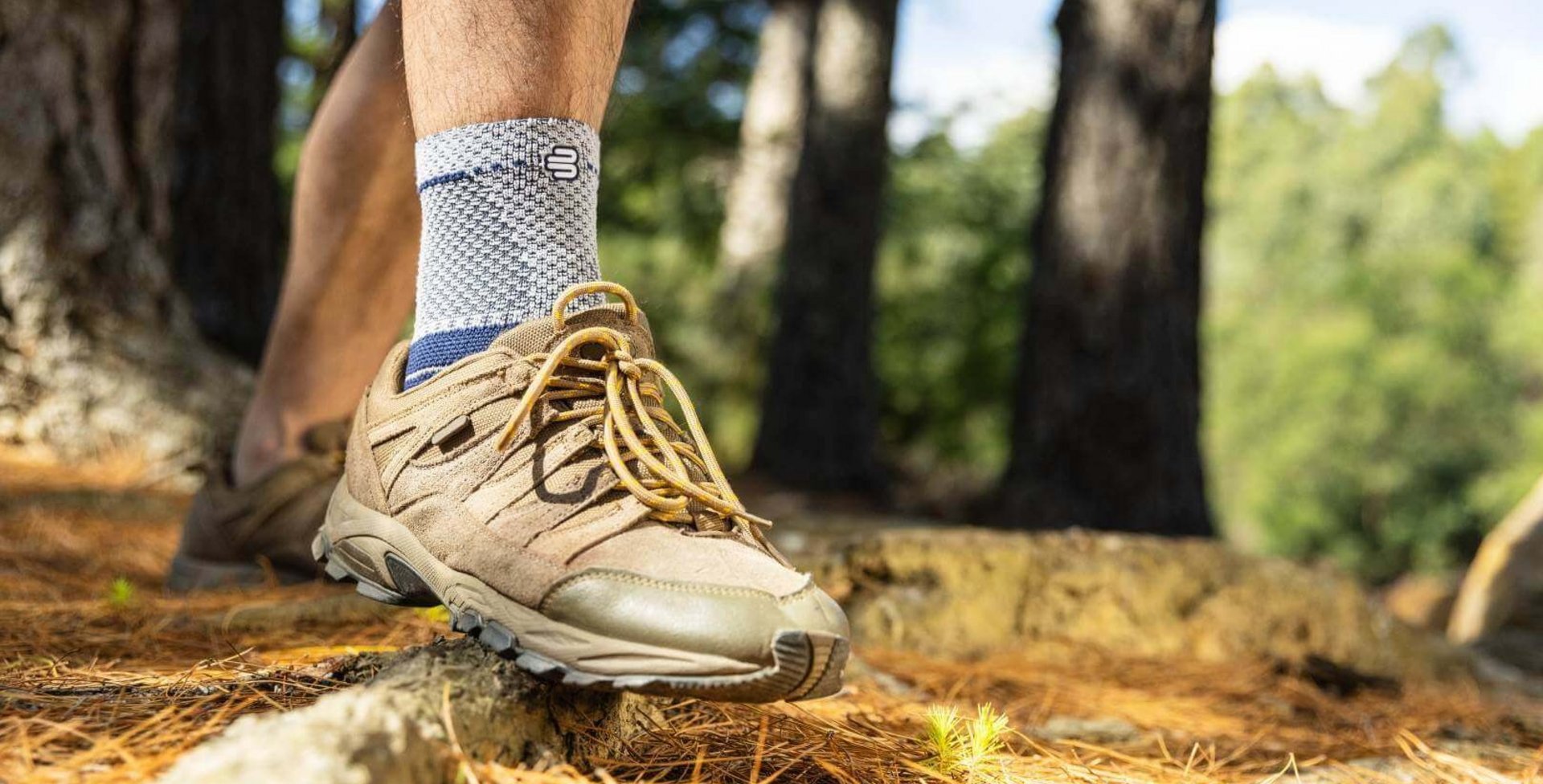 Uitsnede van een wandelaar in het bos die naast wandelschoenen een MalleoTrain bandage aan zijn enkel draagt.