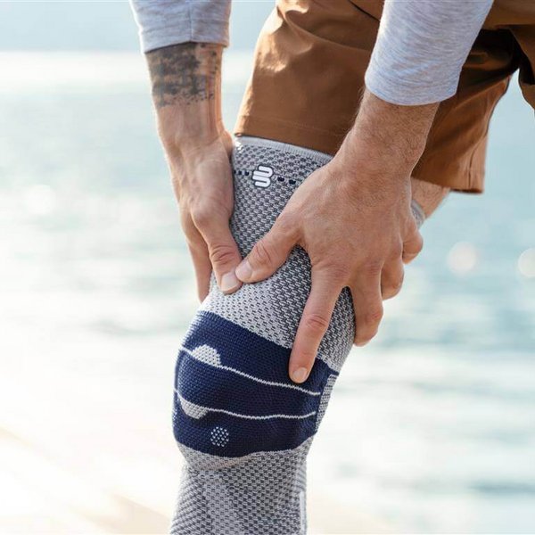 Close-up van de GenuTrain kniebandage. De bandage omsluit de rechterknie en toont een modern, functioneel design. Op de achtergrond is vaag een wateroppervlak te herkennen.