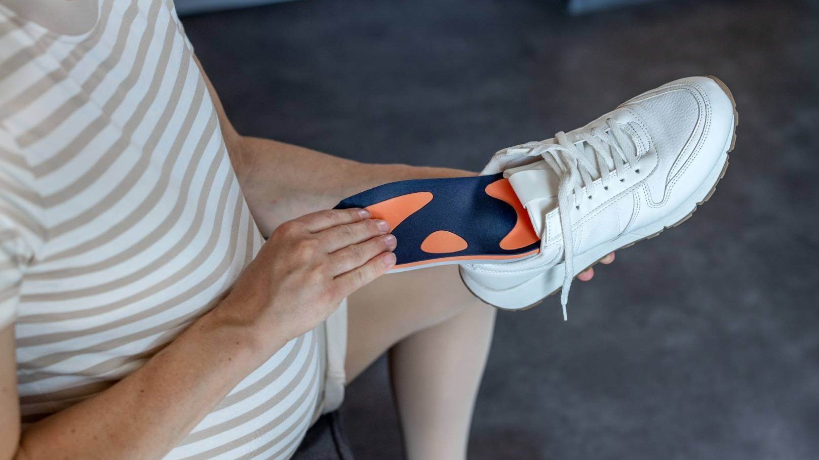 Zwangere vrouw legt een oranje-blauwe inlegzool van Bauerfeind in een witte sneaker. De inlegzool is speciaal afgestemd op de behoeften van zwangere vrouwen, om comfort en ondersteuning bij het lopen te bieden.