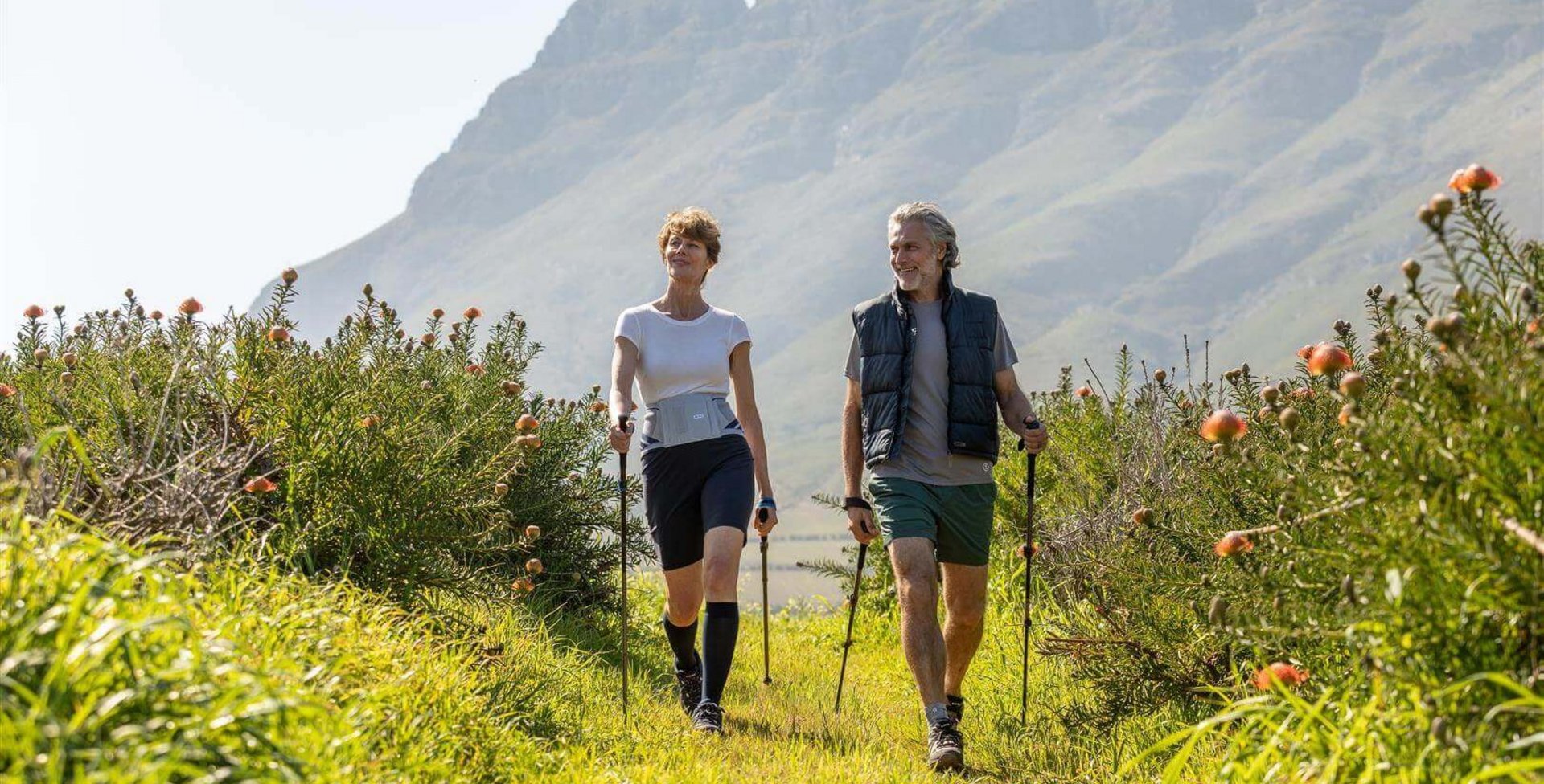Op het beeld zie je hoe een ouder stel in de natuur aan nordic walking doet. Ze dragen Train-bandages van Bauerfeind om hun gewrichten en rug tijdens het bewegen te ontlasten.