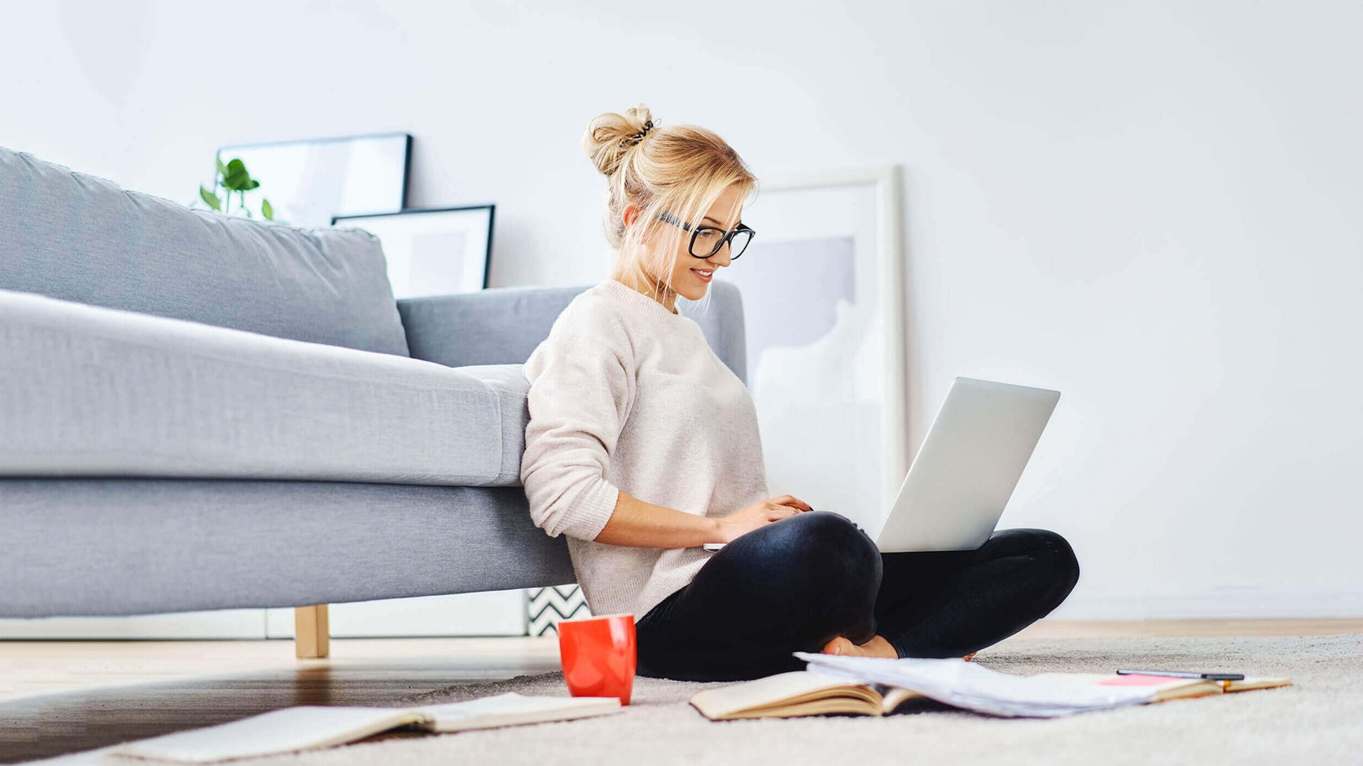 De afbeelding toont een jonge vrouw die met haar laptop op de vloer van haar woning zit en werkt.