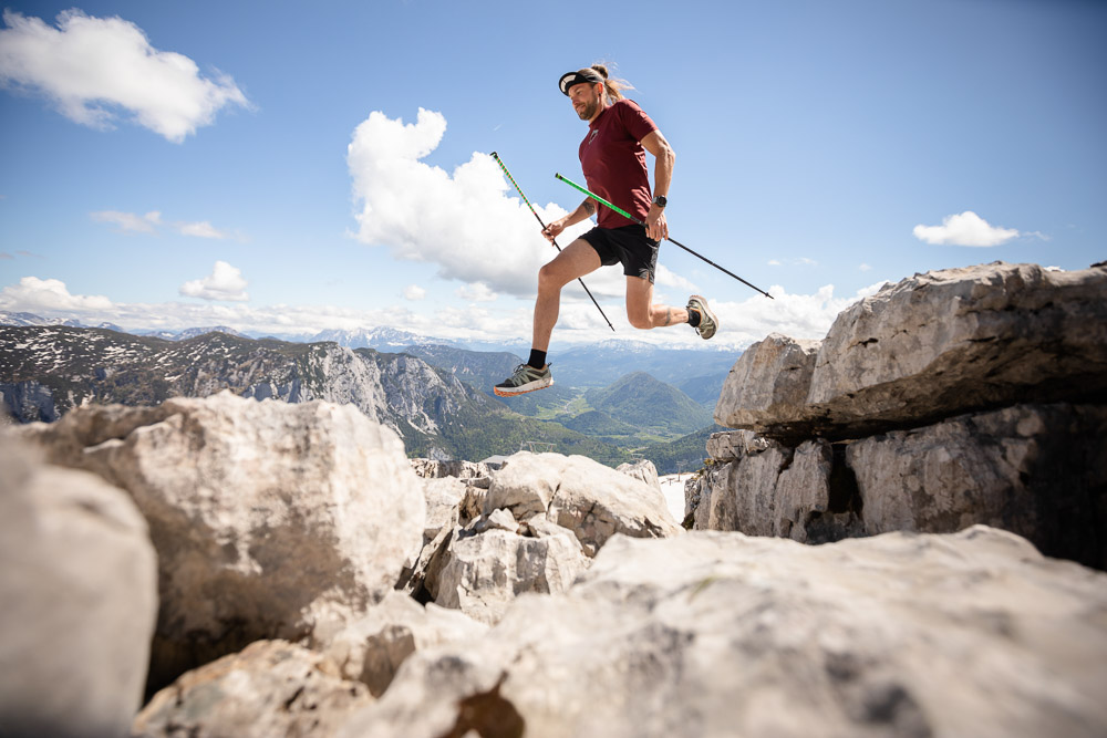 Lord Jens Kramer tijdens het trailrunnen met stokken en een sprong over rotsen in het hooggebergte