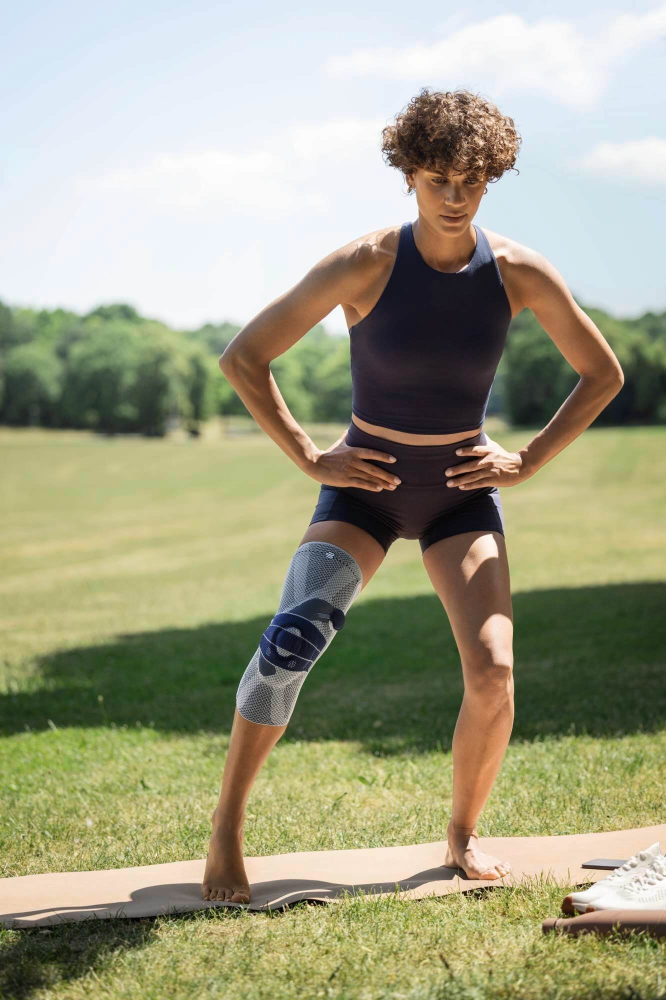 Een vrouw in het park doet bewegingsoefeningen met een kniebandage.